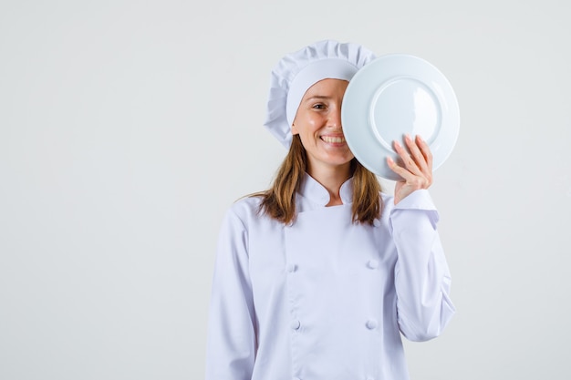 Chef mujer en uniforme blanco sosteniendo la placa cerca de la cara y mirando contenta