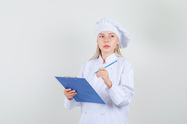 Chef mujer en uniforme blanco sosteniendo el portapapeles y lápiz y mirando ocupado