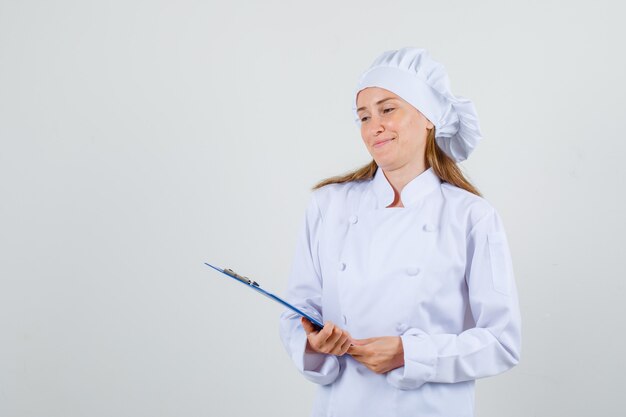 Chef mujer en uniforme blanco sosteniendo portapapeles y sonriendo