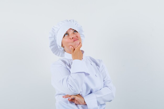 Chef mujer en uniforme blanco sosteniendo su barbilla y mirando pensativo