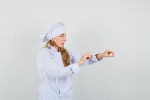 Chef mujer en uniforme blanco subiendo la manga y mirando con cuidado