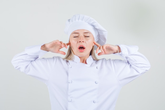 Chef mujer en uniforme blanco tapando las orejas con los dedos y mirando molesto