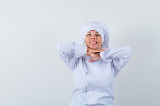 Chef mujer en uniforme blanco tomados de la mano debajo de la barbilla y luciendo lindo