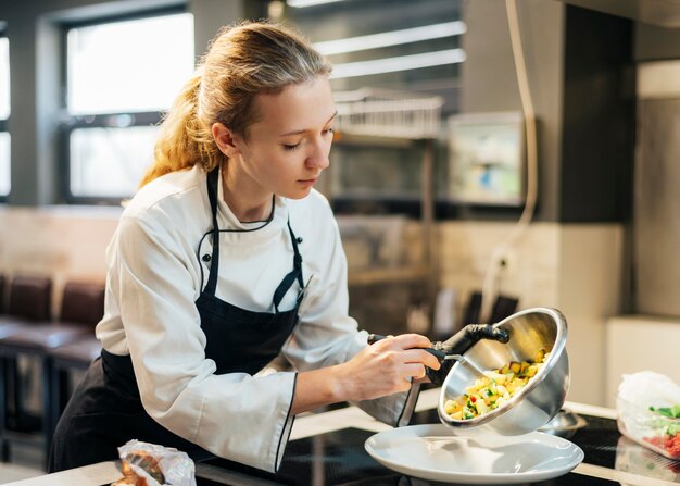 Chef mujer vertiendo comida en la placa