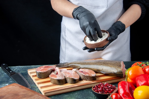 Chef mujer vista frontal con delantal espolvorear harina en rodajas de pescado crudo en la mesa de la cocina