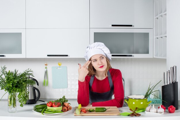 Chef mujer vista frontal en sombrero de cocinero poniendo pistola de dedo en su sien