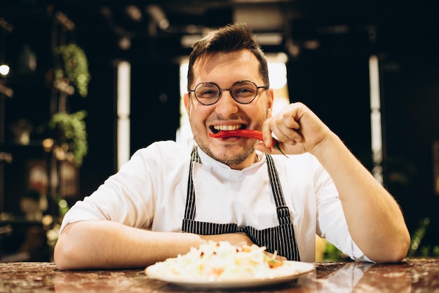 Chef parado junto al mostrador sirviendo ensalada de repollo y sosteniendo guindilla