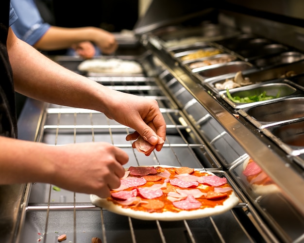 Chef pone salami en masa de pizza cubierta con salsa de tomate