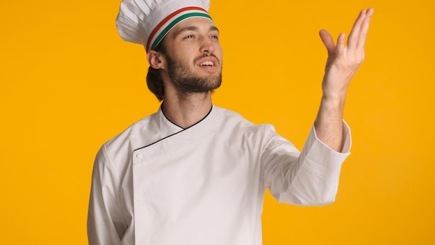 Chef profesional que muestra un delicioso gesto con uniforme aislado en un fondo colorido Hombre atractivo con sombrero de chef que parece inspirado posando en la cámara en el estudio