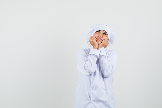 Chef de sexo femenino que almohadilla la cara en sus manos en uniforme blanco y parece esperanzada