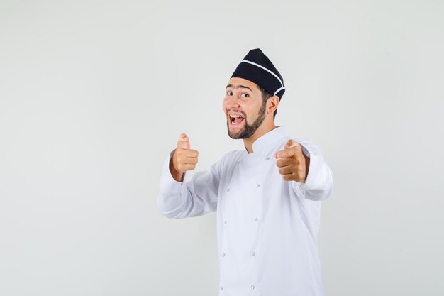 Chef de sexo masculino en uniforme blanco apuntando a vino y mirando positivo, vista frontal.