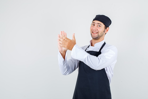 Chef de sexo masculino en uniforme, delantal aplaudiendo después del servicio y mirando alegre, vista frontal.