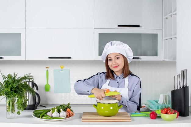 Chef sonriente y verduras frescas con equipo de cocina y tapando la olla en la cocina blanca