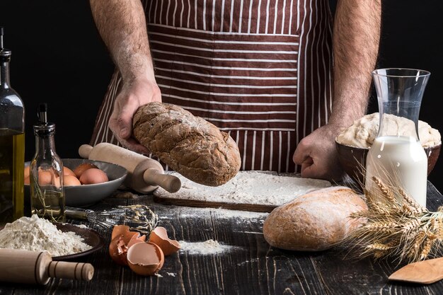 Chef tiene el pan fresco en la mano. Hombre preparando masa en la mesa de la cocina. Sobre fondo negro. Concepto saludable o de cocina.