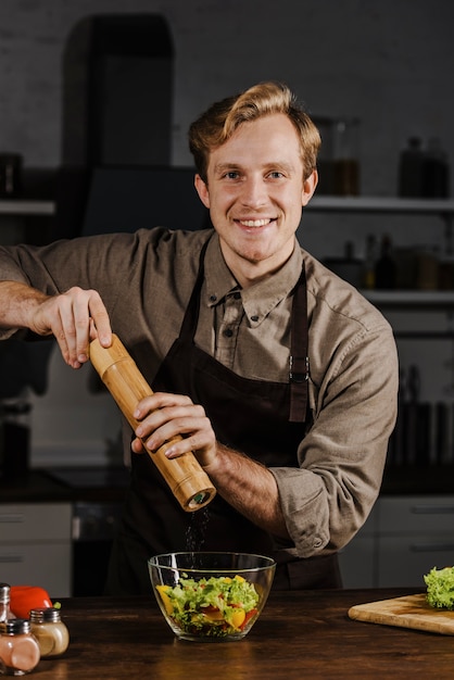 Chef de tiro medio agregando pimienta a la ensalada