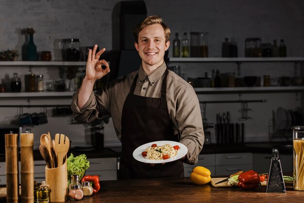 Chef de tiro medio sosteniendo un plato con pasta y haciendo el signo de ok