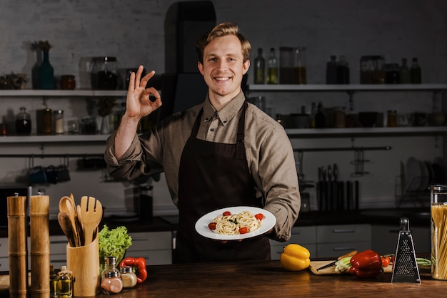 Chef de tiro medio sosteniendo un plato con pasta y haciendo el signo de ok