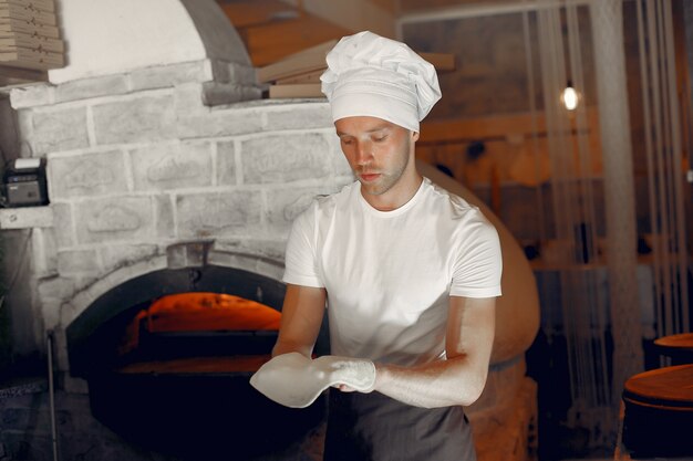 Chef en uniforme blanco prepara una pizzaa