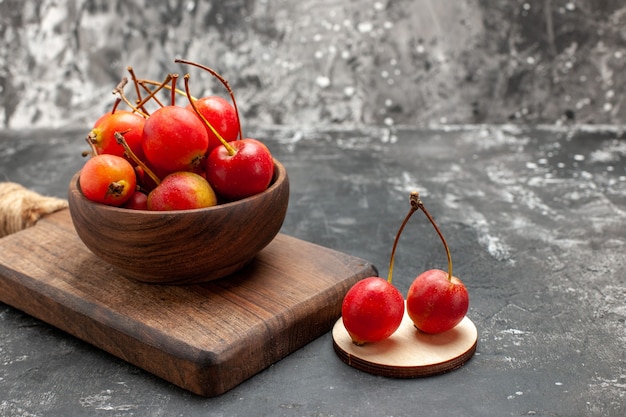 Cheries rojas frescas en un recipiente marrón sobre una pequeña tabla de cortar