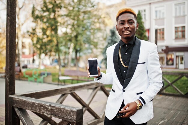 Chic guapo afroamericano en traje blanco con teléfono móvil a mano