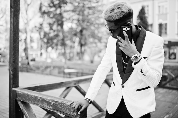 Foto gratuita chic guapo afroamericano en traje blanco con teléfono móvil a mano