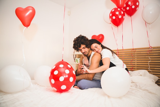 Chica abrazando a su novio desde atrás en una cama