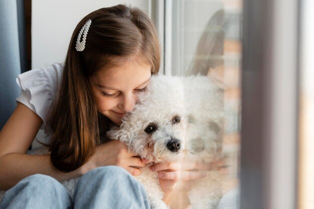 Chica abrazando a su perro junto a una ventana