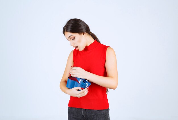 Chica abriendo una caja de regalo azul y se sorprende.