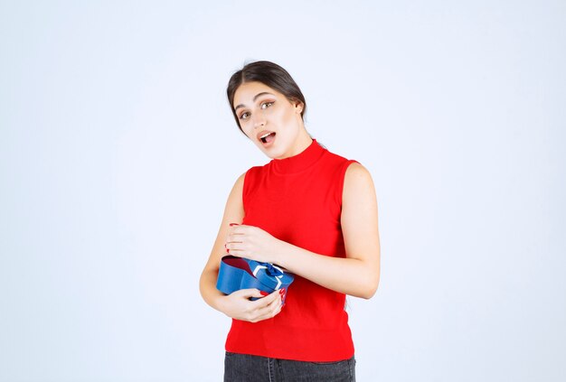 Chica abriendo una caja de regalo azul y se sorprende.