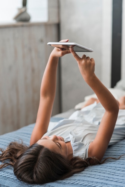 Chica acostada en la cama tocando la pantalla de la tableta digital con el dedo