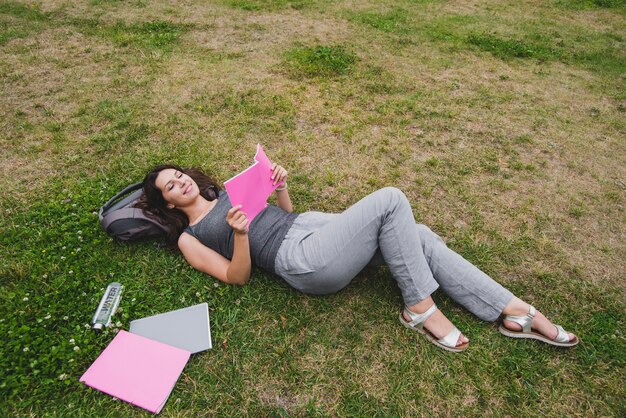 Chica acostado en el cuaderno de lectura de hierba