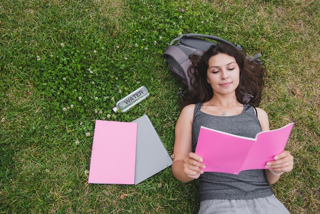 Foto gratuita chica acostado en el cuaderno de lectura de hierba