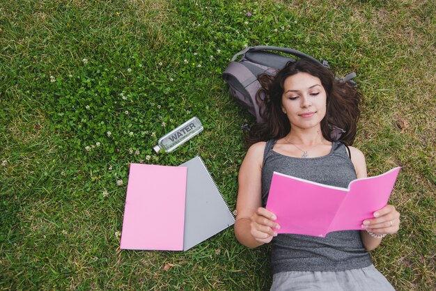 Chica acostado en el cuaderno de lectura de hierba