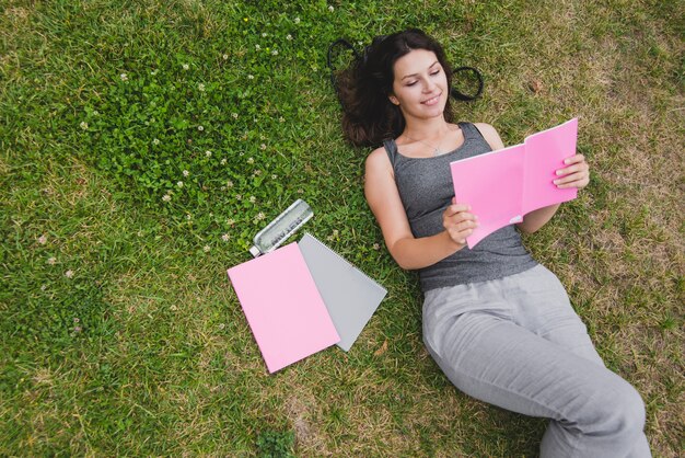Chica acostado en el cuaderno de lectura de hierba