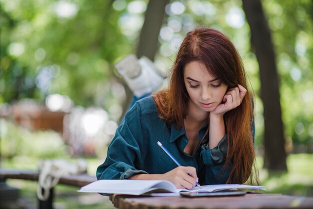 Chica acostado en la mesa en el parque de la escritura