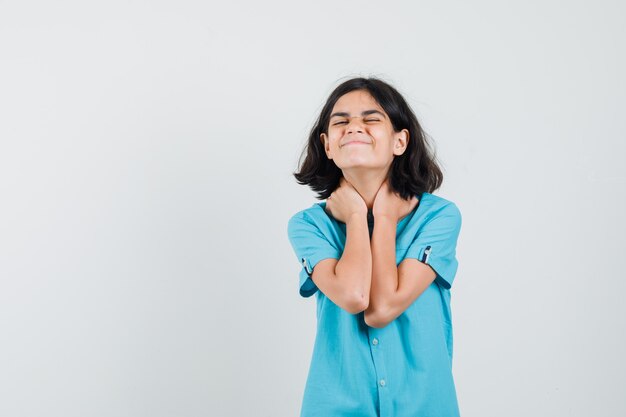 Chica adolescente abrazando su cuello con camisa azul y mirando alegre.