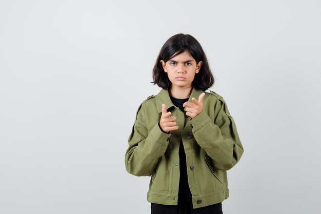 Chica adolescente apuntando hacia adelante con chaqueta verde militar y mirando triste. vista frontal.