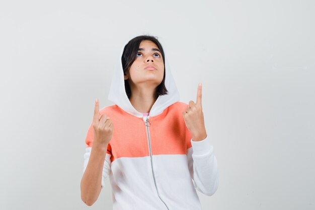 Chica adolescente apuntando hacia arriba en la chaqueta y mirando con cuidado.