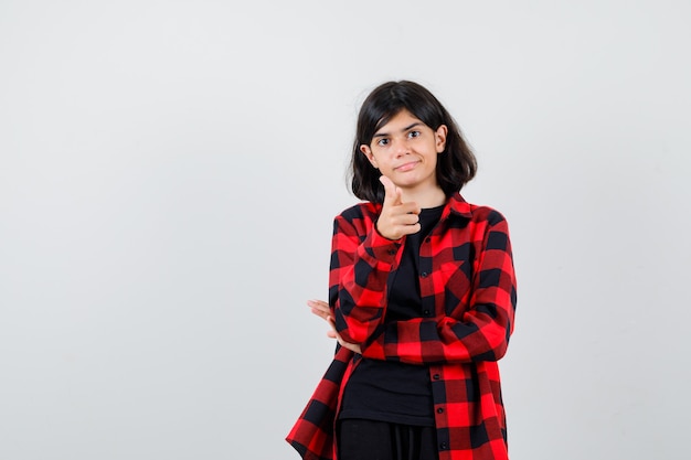 Chica adolescente apuntando con camisa casual y mirando feliz, vista frontal.