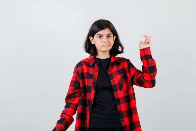 Chica adolescente apuntando a un lado en camiseta, camisa a cuadros y mirando insatisfecho, vista frontal.