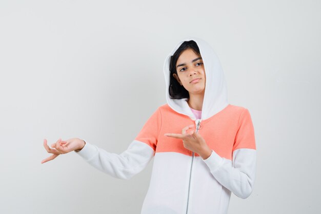 Chica adolescente apuntando a un lado con chaqueta blanca y mirando tranquilo.