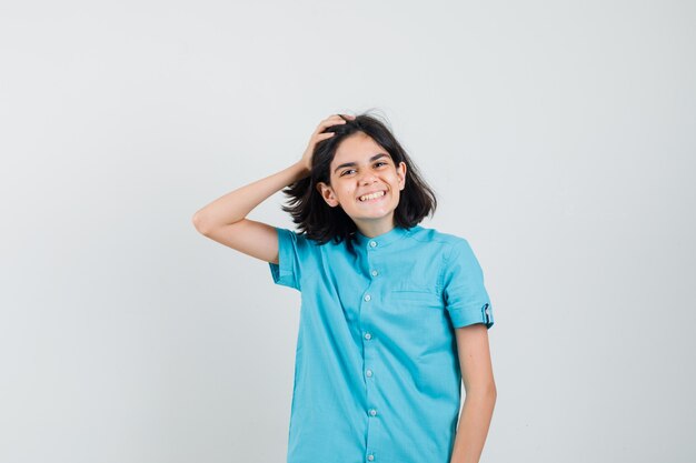 Chica adolescente con camisa azul sosteniendo la mano en la cabeza mientras posa y parece optimista