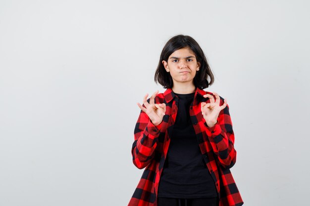 Chica adolescente en camisa casual mostrando signo ok y mirando vacilante, vista frontal.