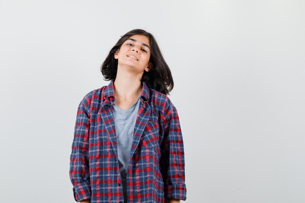 Chica adolescente en camisa a cuadros y mirando complacido, vista frontal.