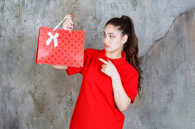 Chica adolescente en camisa roja sosteniendo una bolsa roja y parece confundida y pensativa.