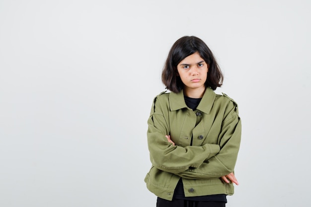 Foto gratuita chica adolescente en camiseta, chaqueta de pie con los brazos cruzados y mirando imprudente, vista frontal.
