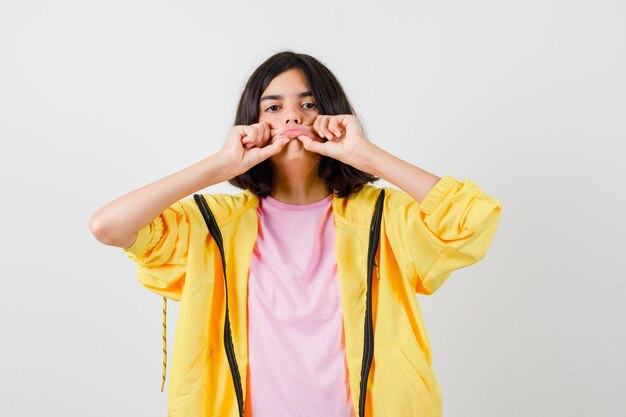 Chica adolescente en chándal amarillo, camiseta sosteniendo y estirando sus labios y mirando nostálgico, vista frontal.