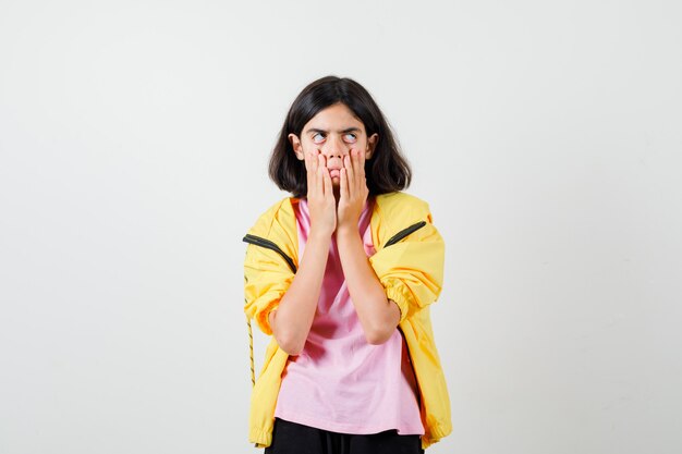 Chica adolescente en chándal amarillo, camiseta tirando de ella boca abajo y mirando insatisfecho, vista frontal.