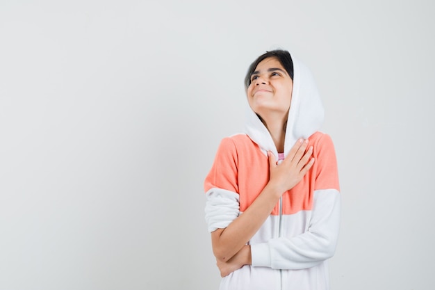 Foto gratuita chica adolescente con chaqueta blanca sosteniendo la mano sobre su pecho y mirando agradecido.