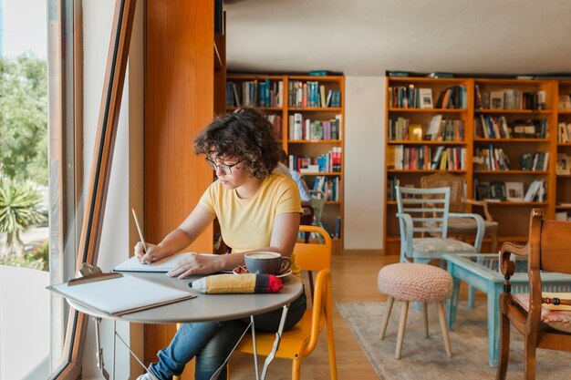 Chica adolescente escribiendo en el cuaderno junto a la ventana